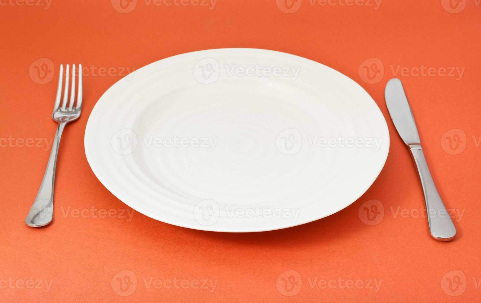 empty white plate with fork and knife set on red photo