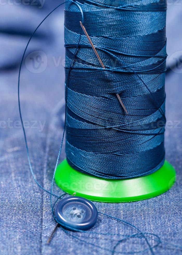 thread bobbin with needle, button on blue cloth photo