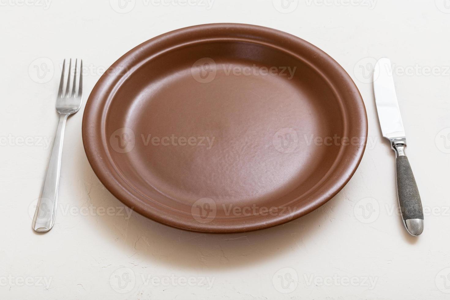 brown plate with knife, spoon on white plaster photo