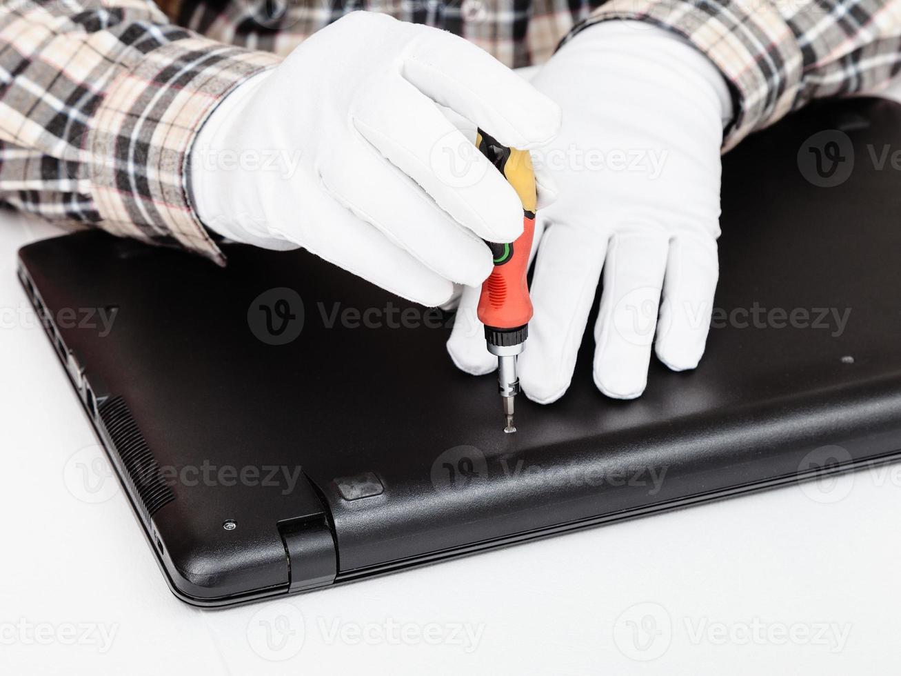 serviceman disassembles laptop with screwdriver photo