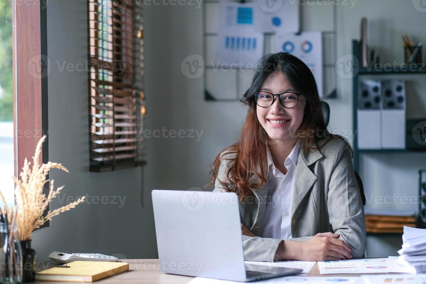 Pretty Asian woman sitting in the office, calculator, working on data, charts and documents on the table in business workspace. Looking camera. photo