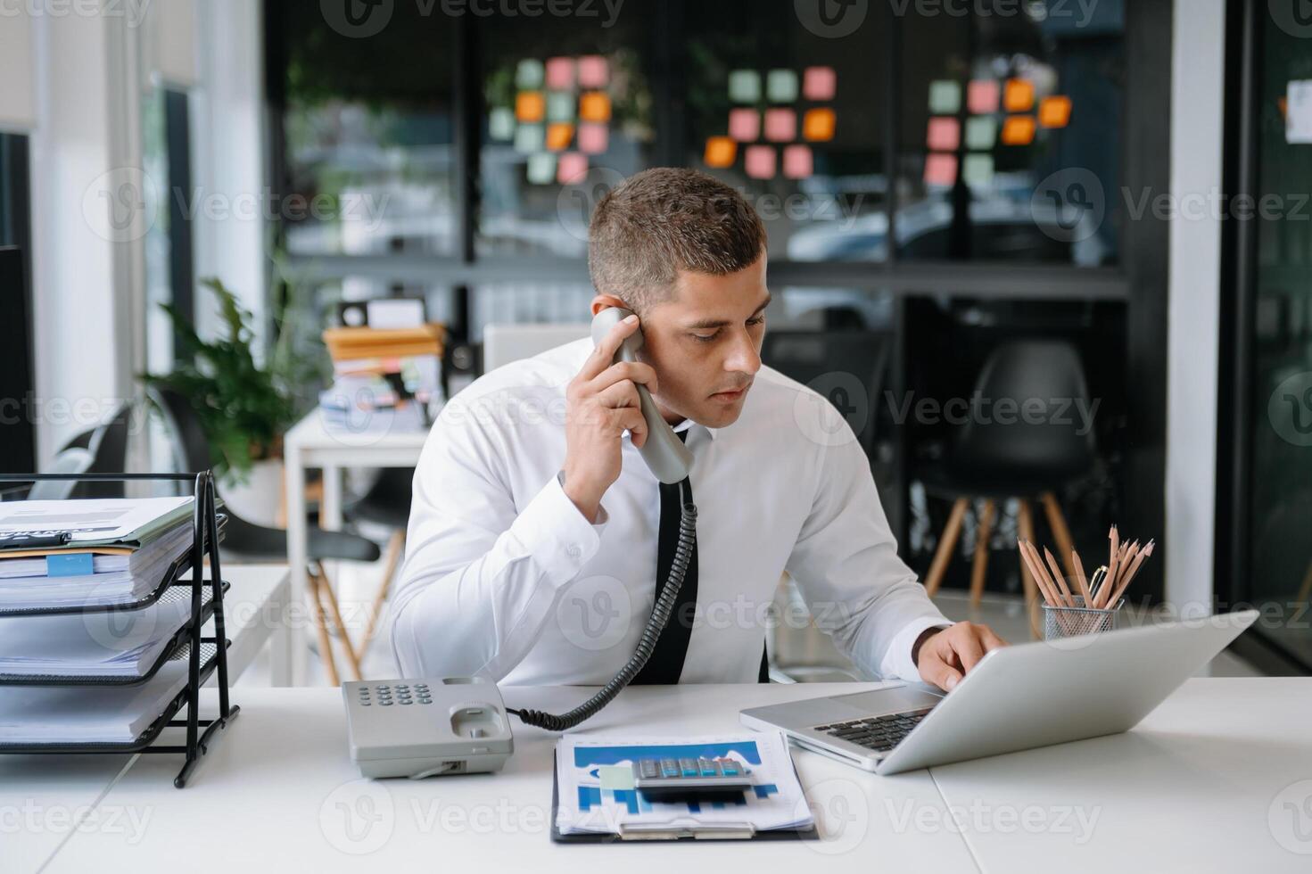 Businessman Talking on the phone and using a laptop with a smile while sitting at office photo
