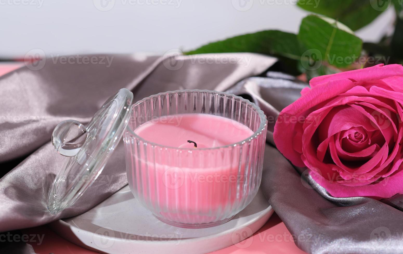 hermosa rosa rosa con vela aromática sobre fondo textil satinado de lujo. foto