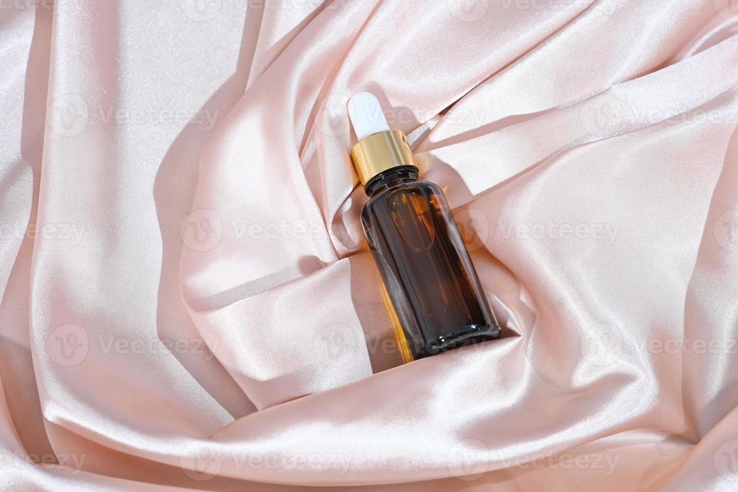 amber glass dropper bottle with cosmetic product on a satin or silk background. beauty face care solution. unbranded brown bittle, anti age female serum. photo