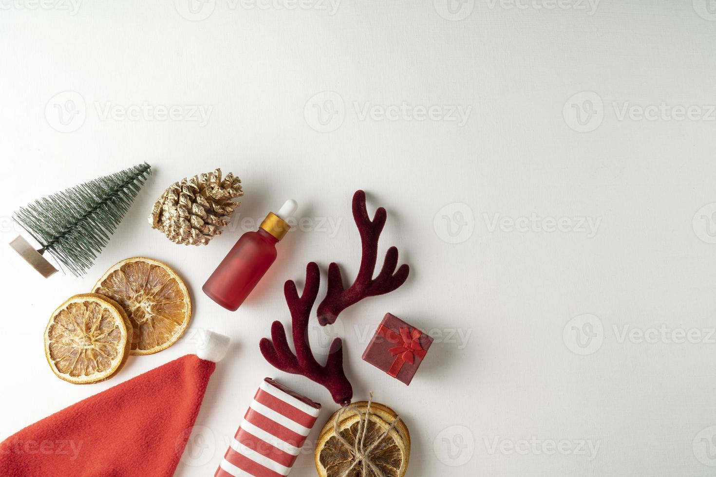 A face serum or essential oil for Christmas holidays in a red dropper bottle lying on a white background with cinnamon and dried oranges around photo