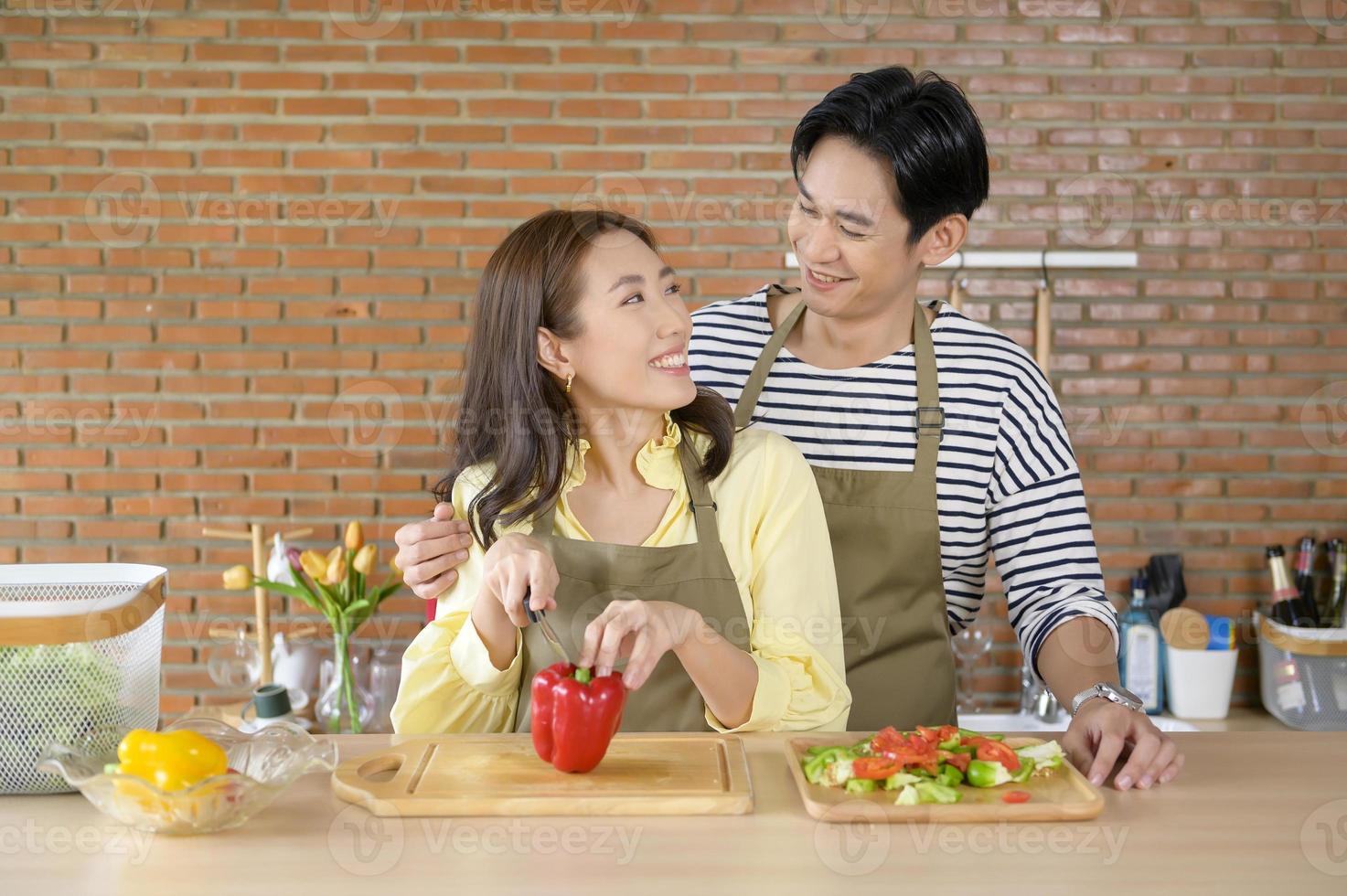 Young smiling asian couple wearing an apron in the kitchen room, cooking concept photo