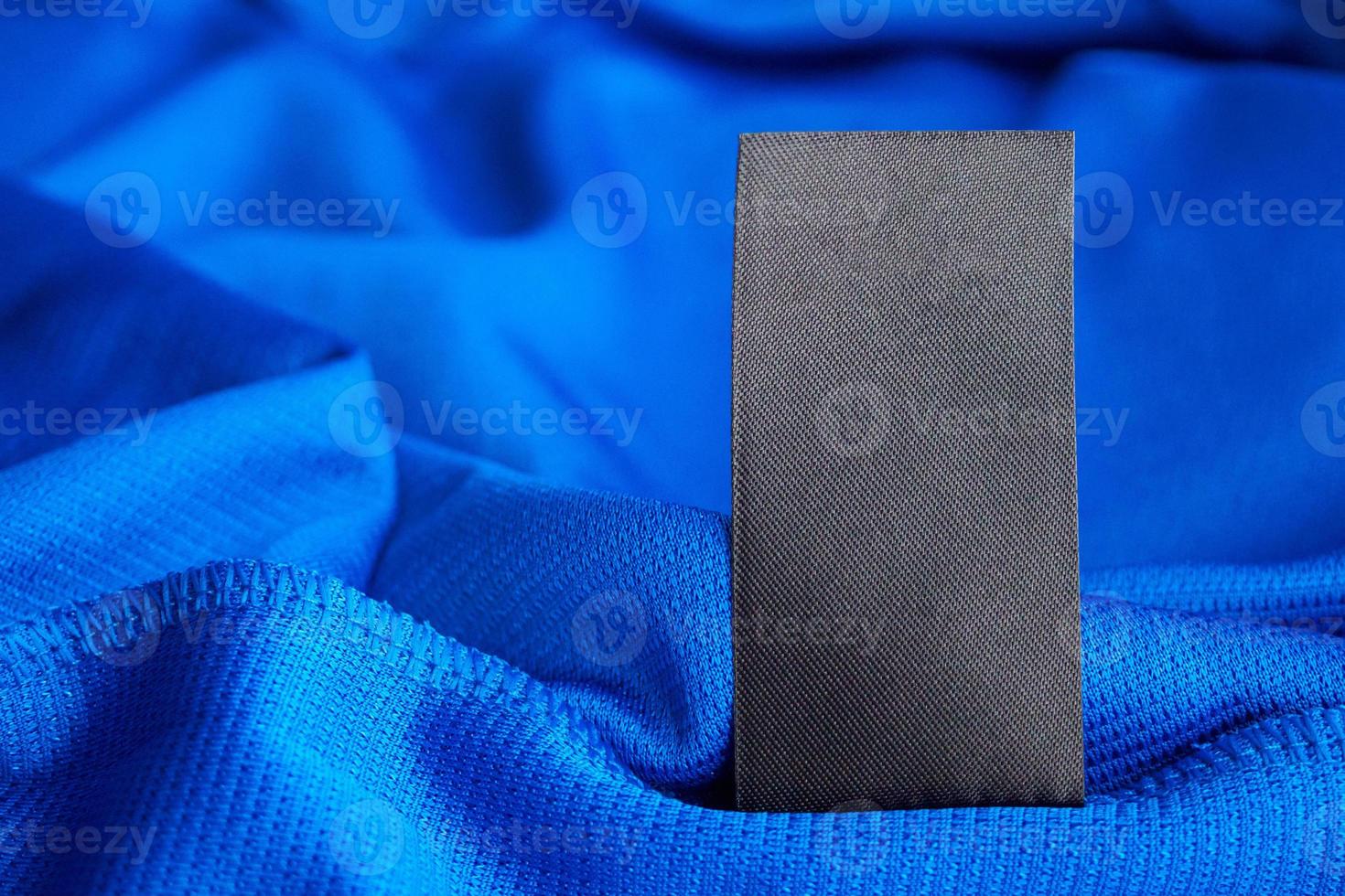 Black blank laundry care clothes label on blue jersey polyester sport shirt background photo