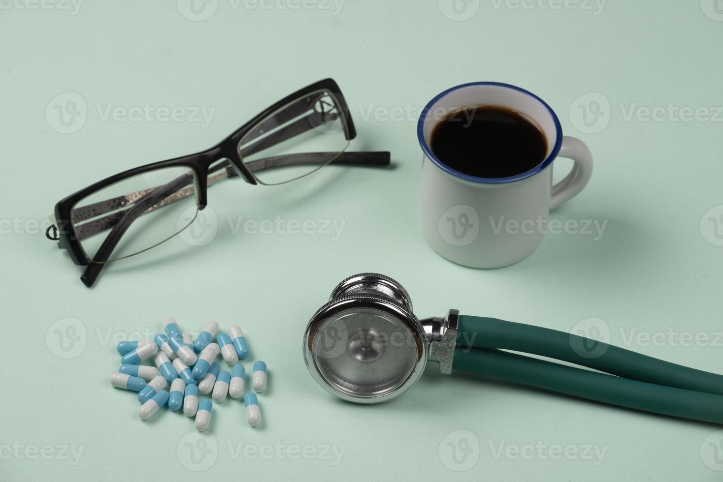 medical object on light green background, with glasses, pills, stethoscope and cup of coffee photo