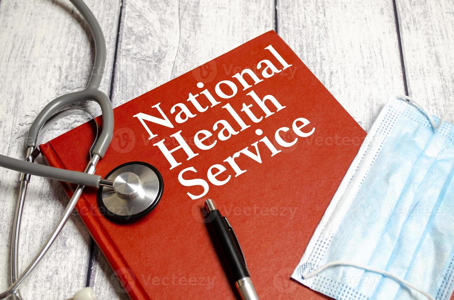 Text NHS National Health Service on red notebook and stethoscope, blue mask and pen photo