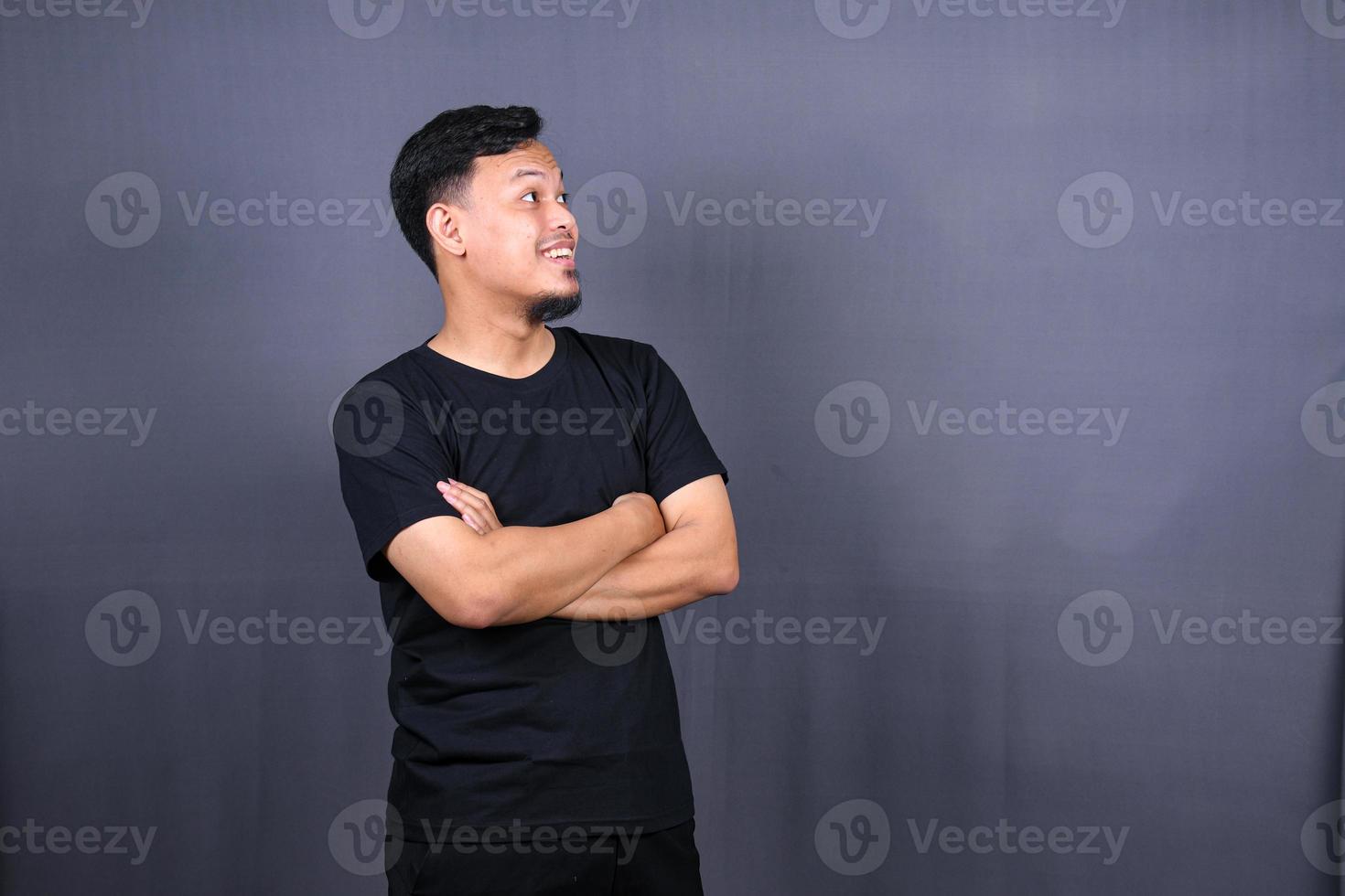 Smiling handsome asian man in black t-shirt standing with crossed arms isolated on gray background photo