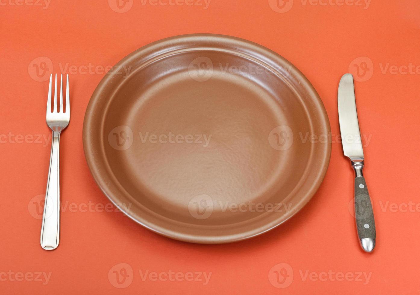 above view of ceramic plate, fork, knife on red photo