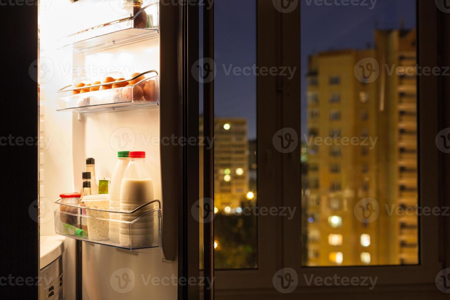 puerta abierta del refrigerador y vista urbana en la noche foto