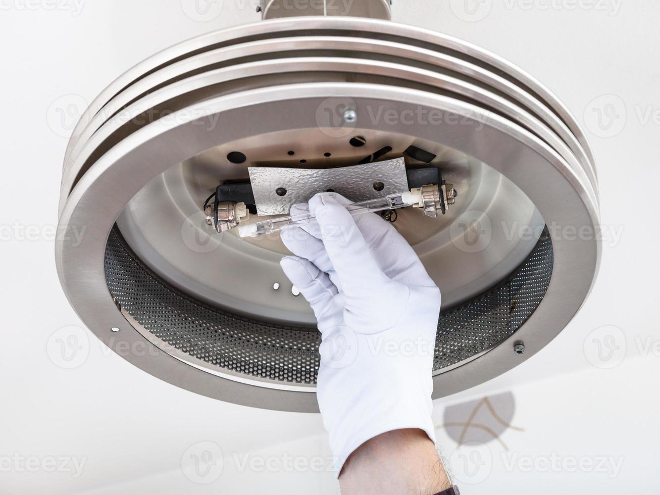 Electrician changing halogen lamp in ceiling light photo