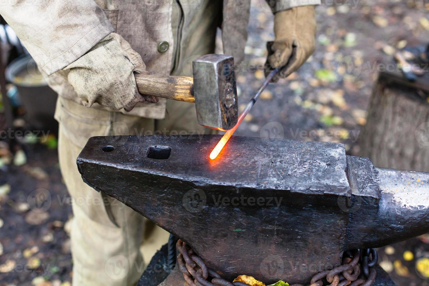herrero martillando varilla de acero caliente en el yunque foto