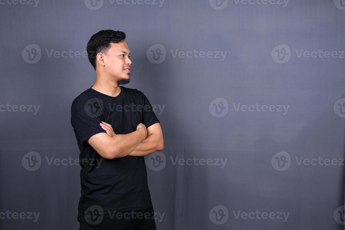 Smiling handsome asian man in black t-shirt standing with crossed arms isolated on gray background photo