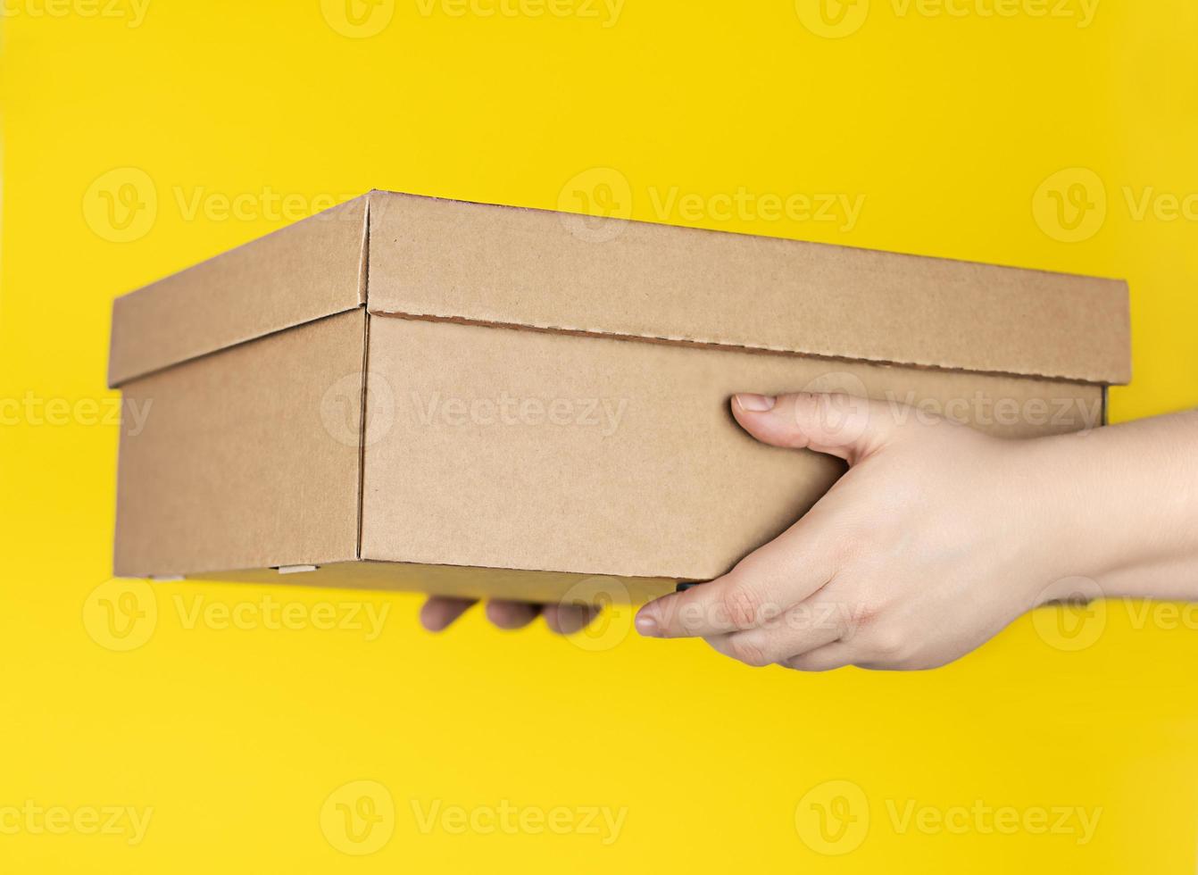 Large cardboard box in hands on a yellow background. photo