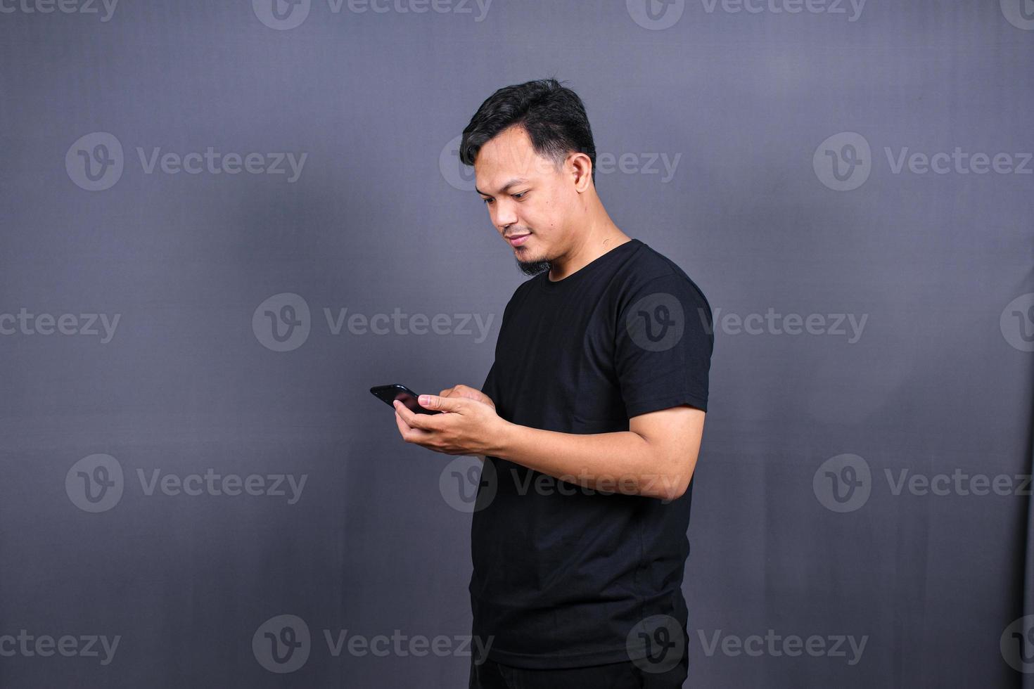 Photo of attractive asian guy holding mobile phone wear black t-shirt isolated gray color background