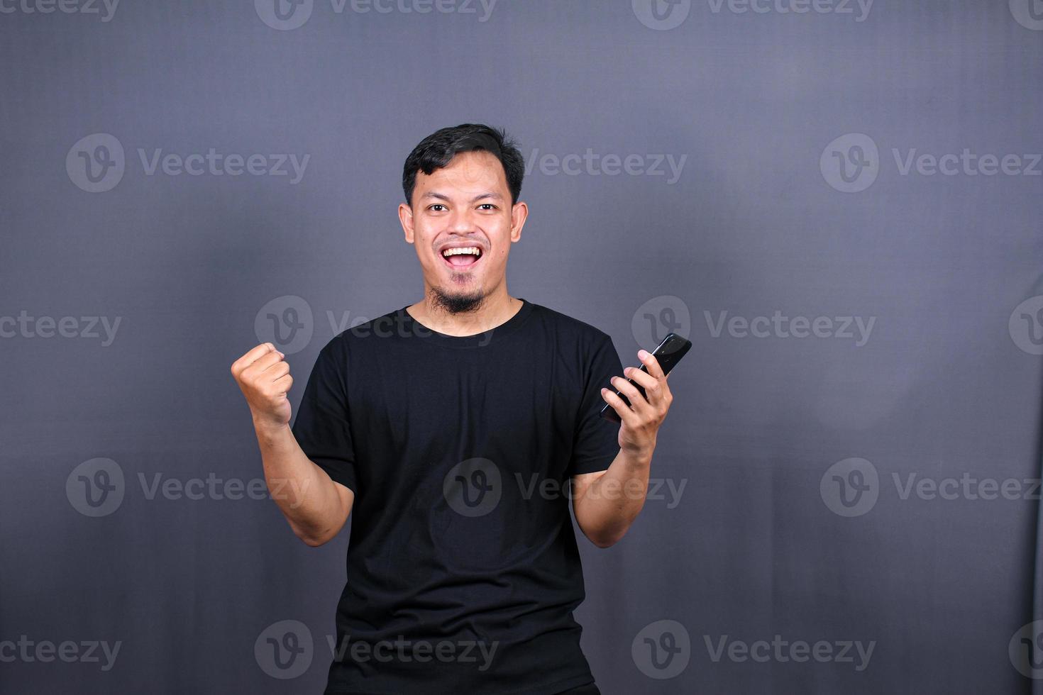 Happy Asian man holding a smartphone and winning the prize. isolated on gray background photo
