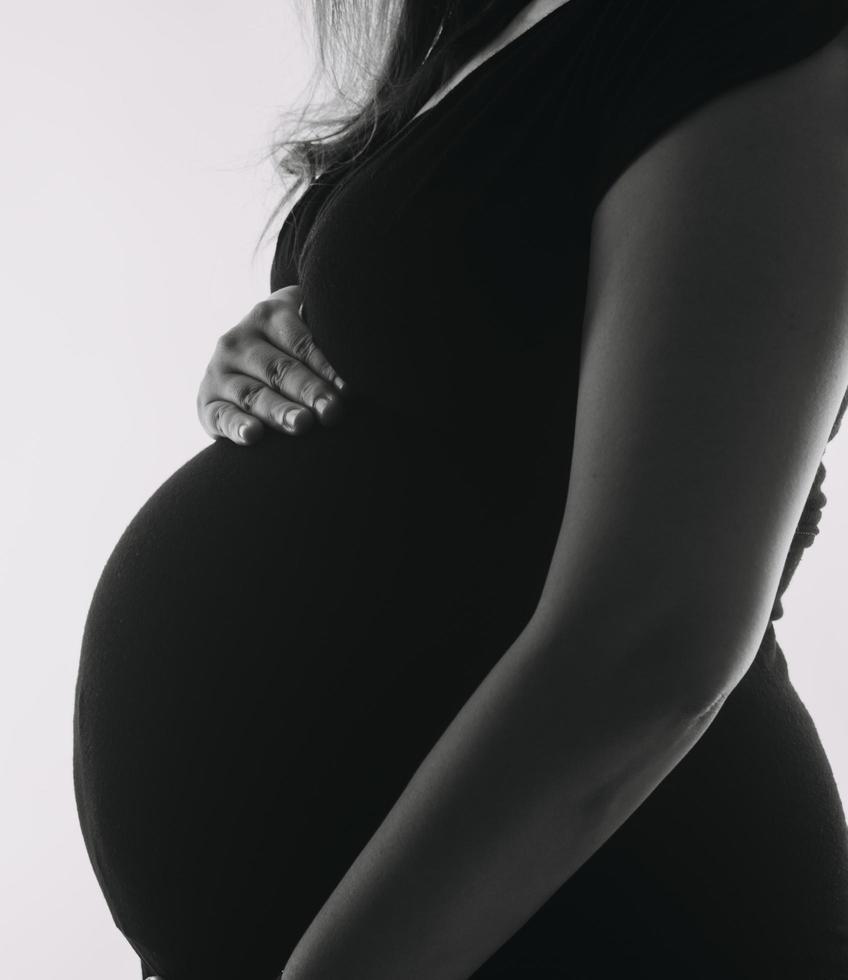 Young adult pregnant woman in white clothes touching big naked belly with hands. Showing shape. Pregnancy concept. Expectation time. Closeup. Isolated on light gray wall background. photo