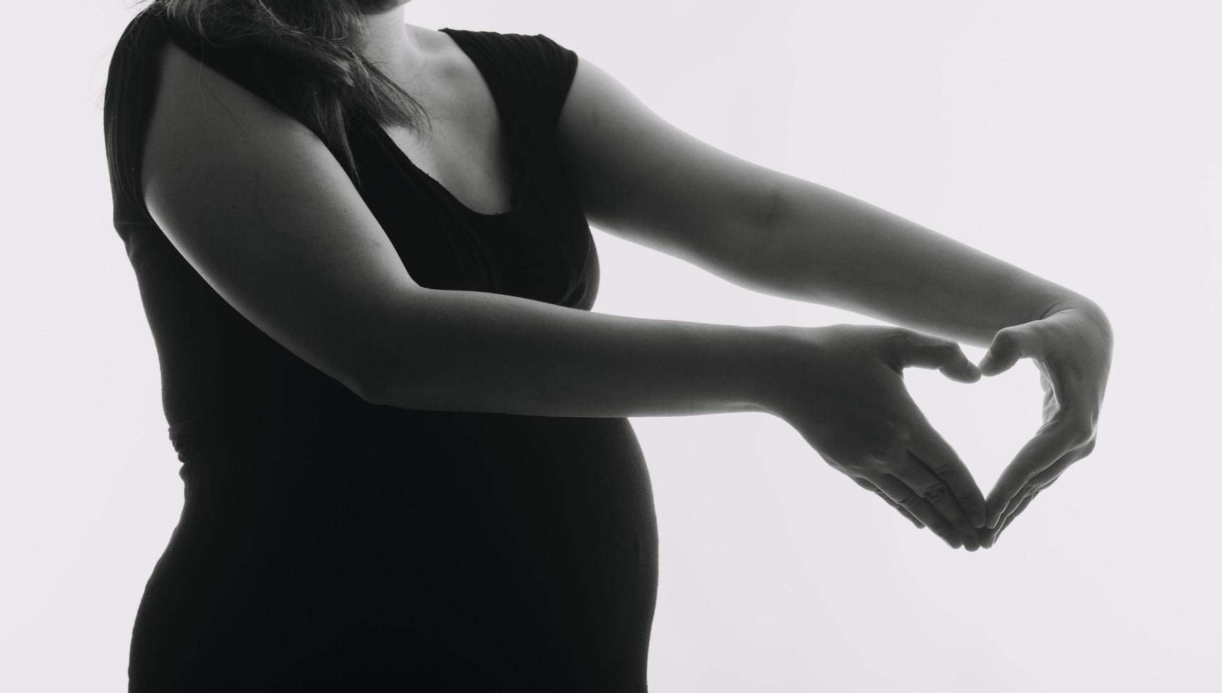 Young adult pregnant woman in white clothes touching big naked belly with hands. Showing shape. Pregnancy concept. Expectation time. Closeup. Isolated on light gray wall background. photo