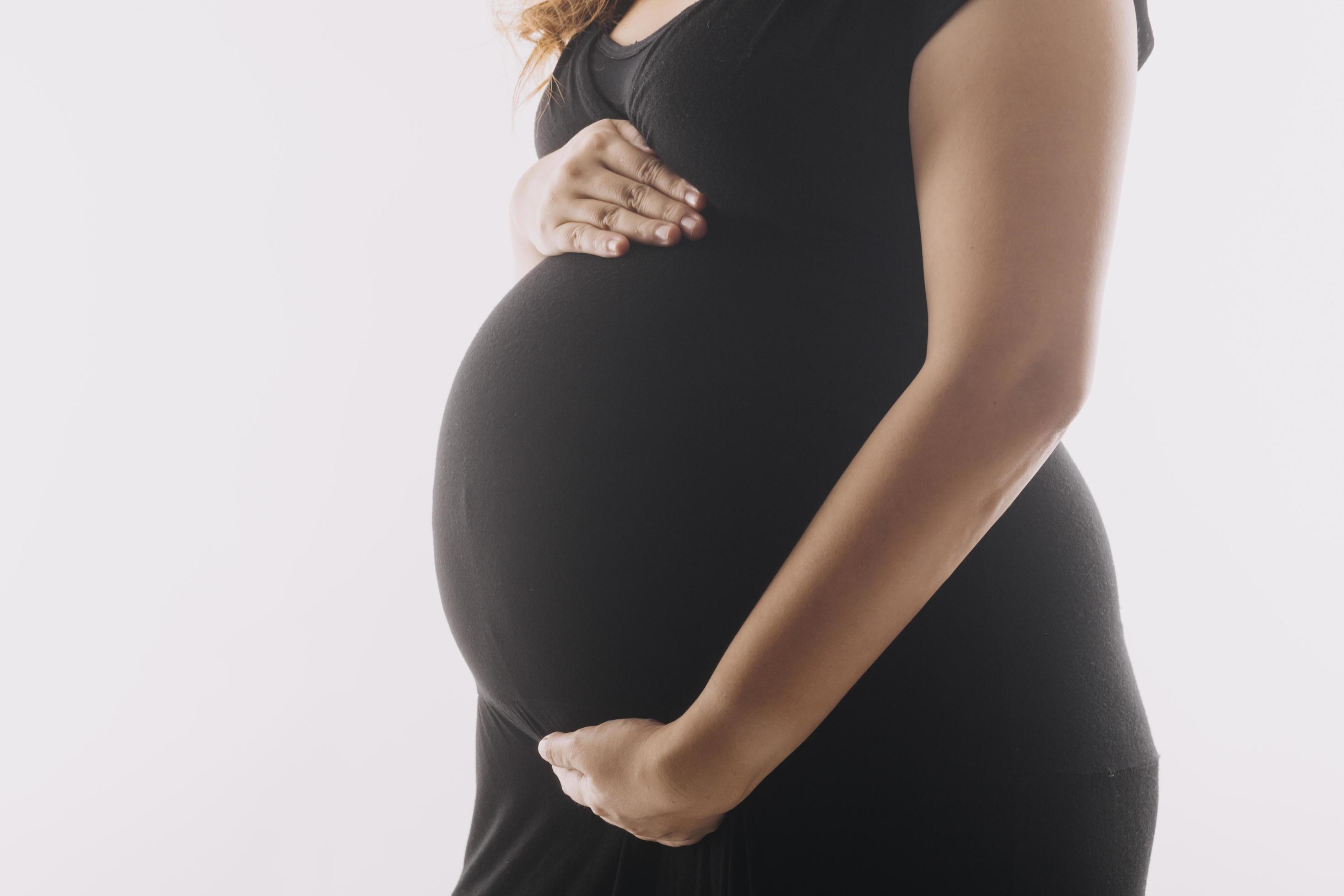 mujer adulta joven embarazada vestida de blanco tocando una gran barriga desnuda con las manos