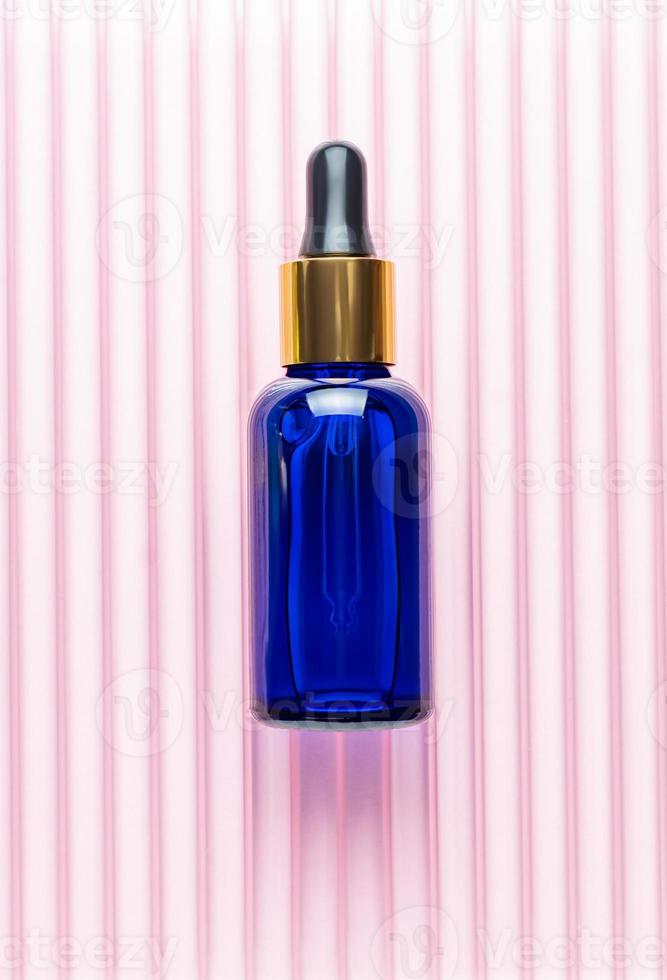 Blue glass dropper bottle with beauty care serum, hyaluronic acid and vitamins on pink background. Home cosmetics and spa concept photo