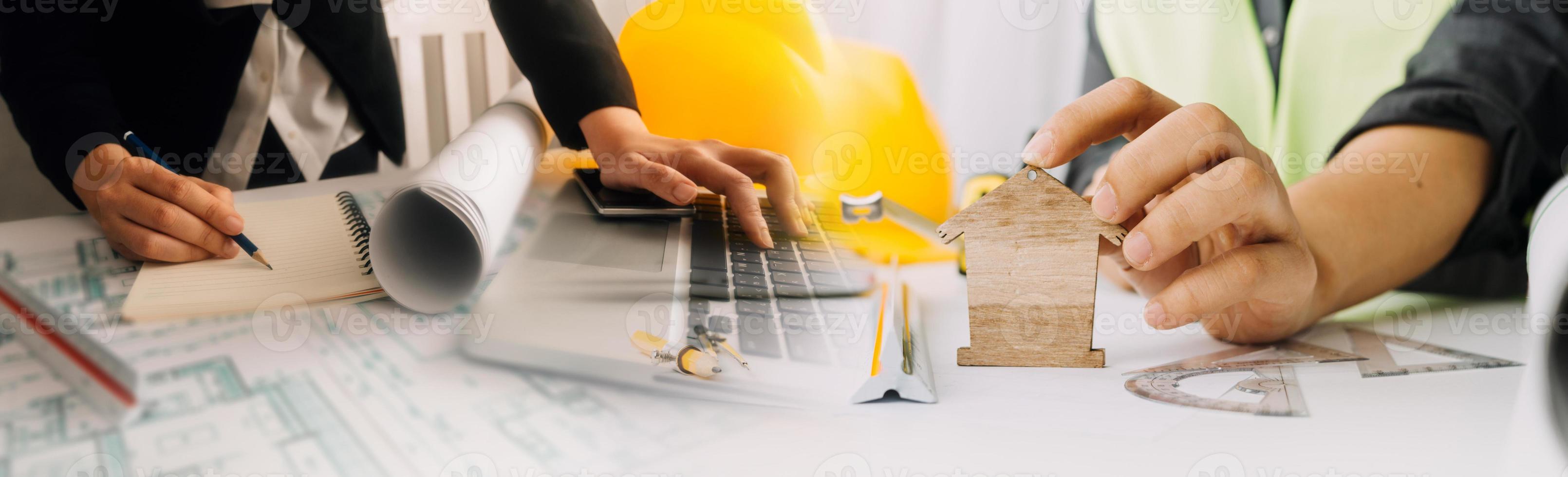 Two colleagues discussing data working and tablet, laptop with on on architectural project at construction site at desk in office photo