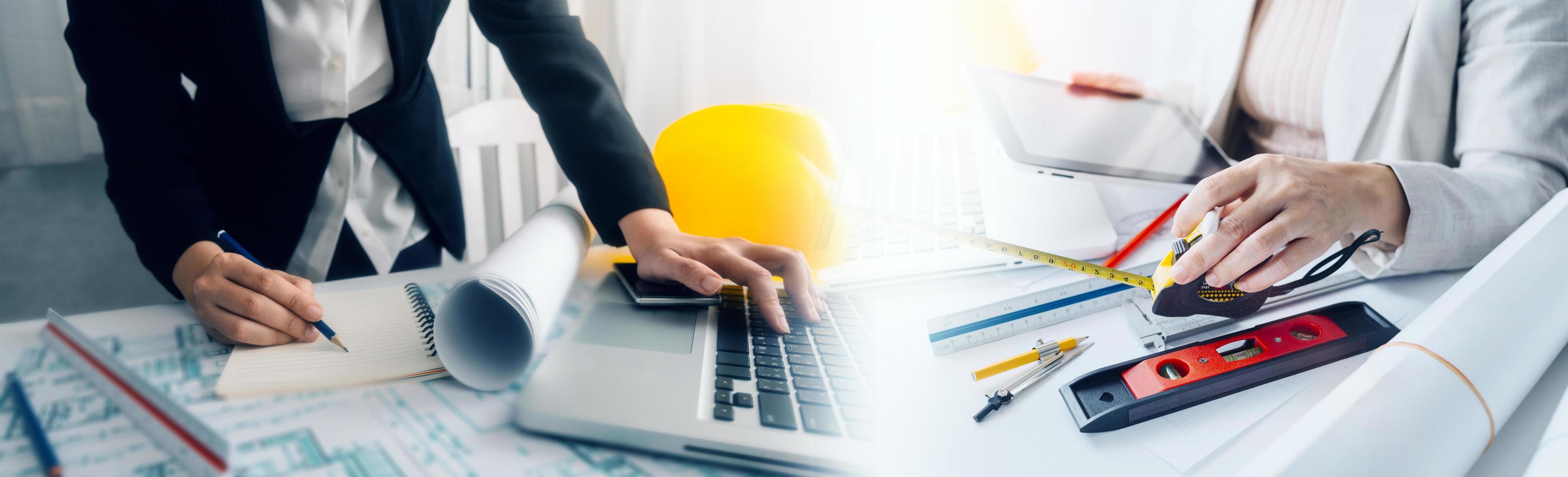 Two colleagues discussing data working and tablet, laptop with on on architectural project at construction site at desk in office photo