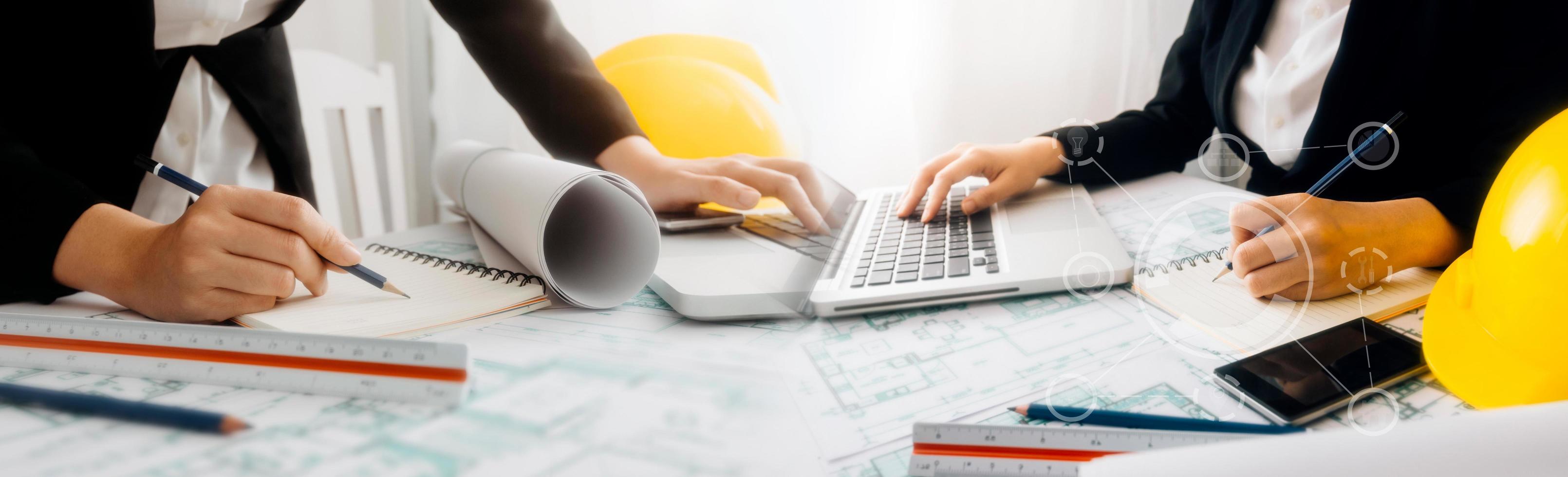 Two colleagues discussing data working and tablet, laptop with on on architectural project at construction site at desk in office photo