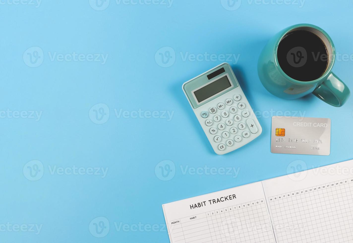 flat lay of habit tracker book,  blue cup of black coffee, blue calculator and credit card on blue background with copy space. Business and good  financial habit photo