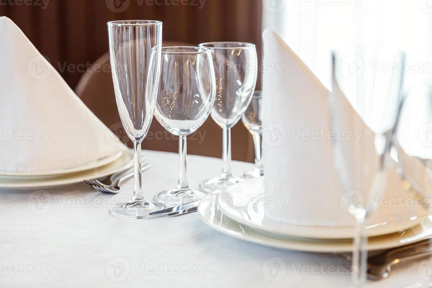 Fancy table set for dinner with napkin glasses in restaurant, luxury interior background. Wedding elegant banquet decoration and items for food arranged by catering service on white tablecloth table. photo