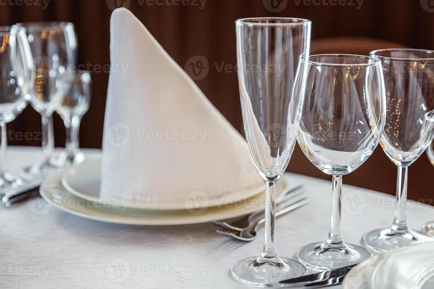 Fancy table set for dinner with napkin glasses in restaurant, luxury interior background. Wedding elegant banquet decoration and items for food arranged by catering service on white tablecloth table. photo