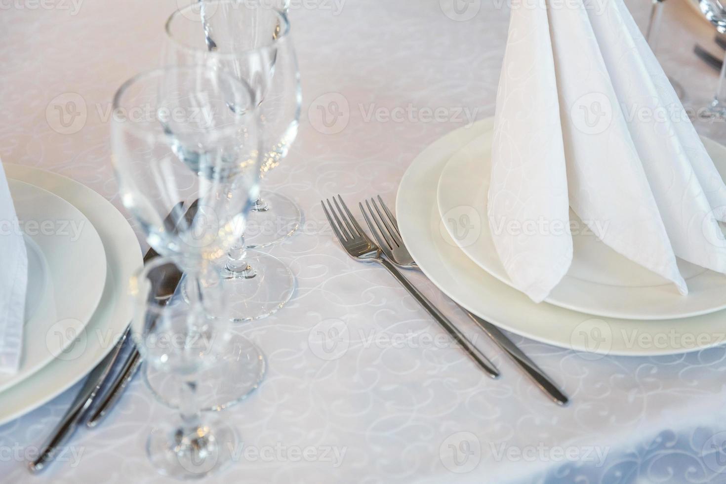 Fancy table set for dinner with napkin glasses in restaurant, luxury interior background. Wedding elegant banquet decoration and items for food arranged by catering service on white tablecloth table. photo
