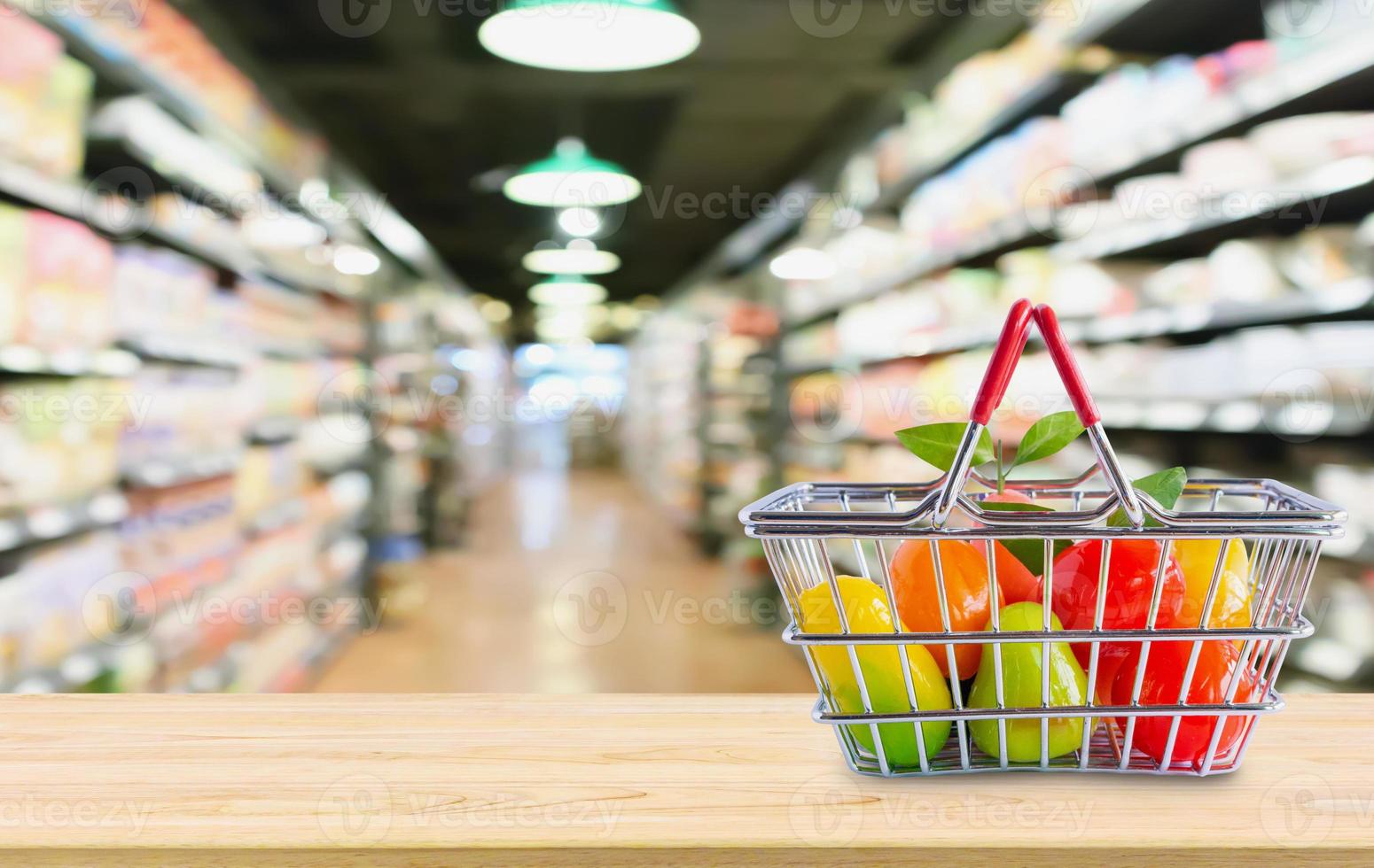 Shopping basket with fruits on wood table over grocery store supermarket blur background photo