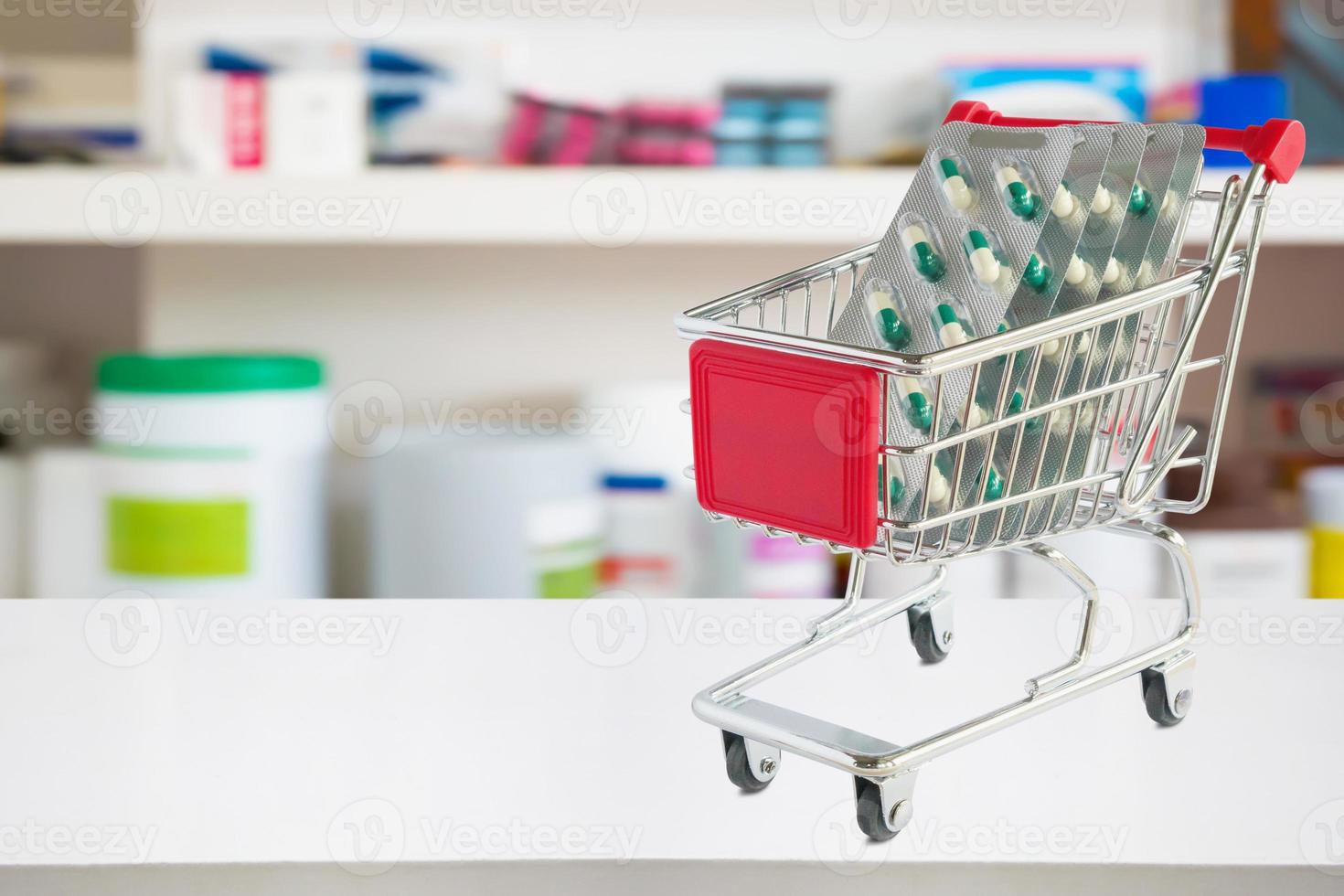 medicine pills capsule in shopping cart on pharmacy store counter with blur drugstore shelves defocused background photo