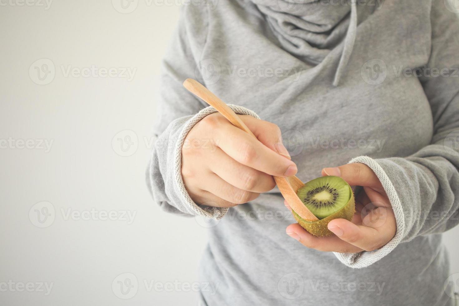 Young female eating ripe kiwi fruit with wooden spoon photo