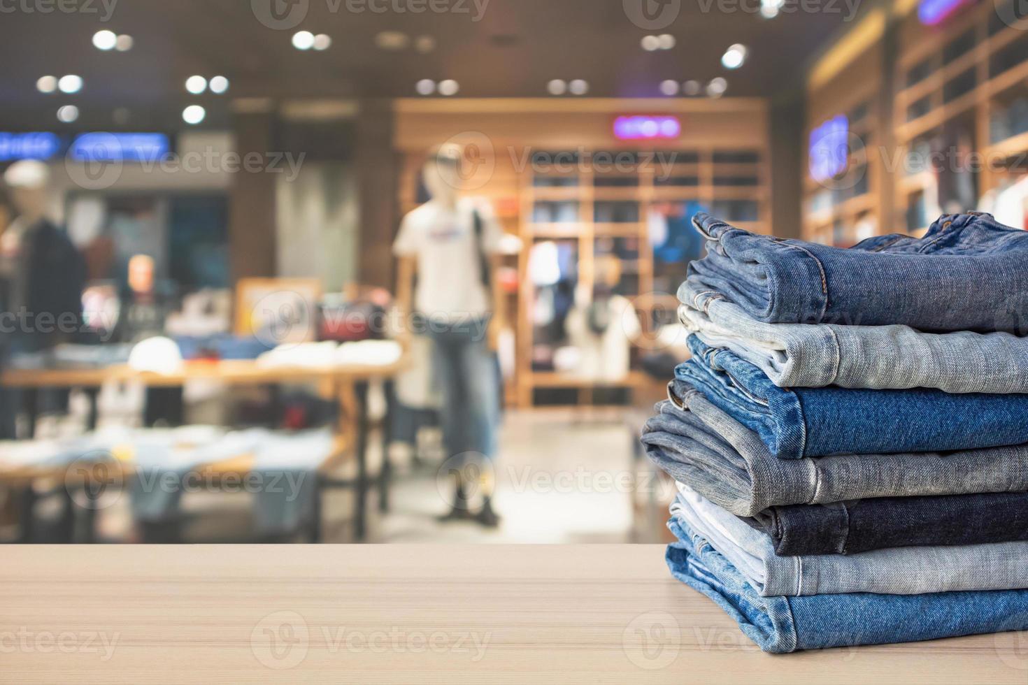 Blue denim jeans stack on wood table top with abstract blur clothing store in modern shopping mall defocused bokeh light background photo