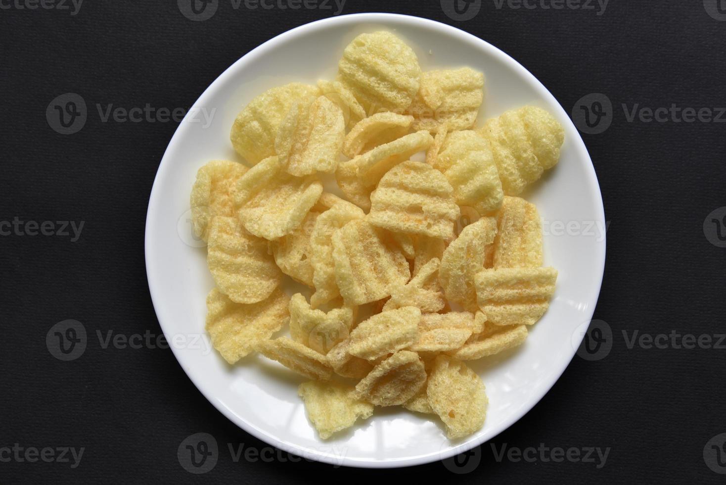 Delicious peppery corn chips on a white plate. Beer appetizer on a plate on a black background. photo