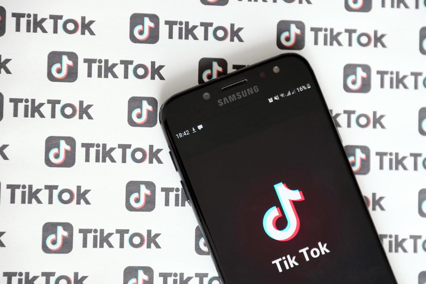 TERNOPIL, UKRAINE - MAY 2, 2022 Tik Tok smartphone app on screen and Many TikTok logo printed on paper. Tiktok or Douyin is a famous Chinese short-form video hosting service owned by ByteDance photo