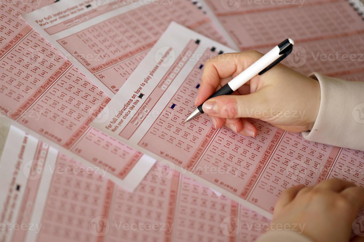 Filling out a lottery ticket. A young woman plays the lottery and dreams of winning the jackpot. Female hand marking number on red lottery ticket photo