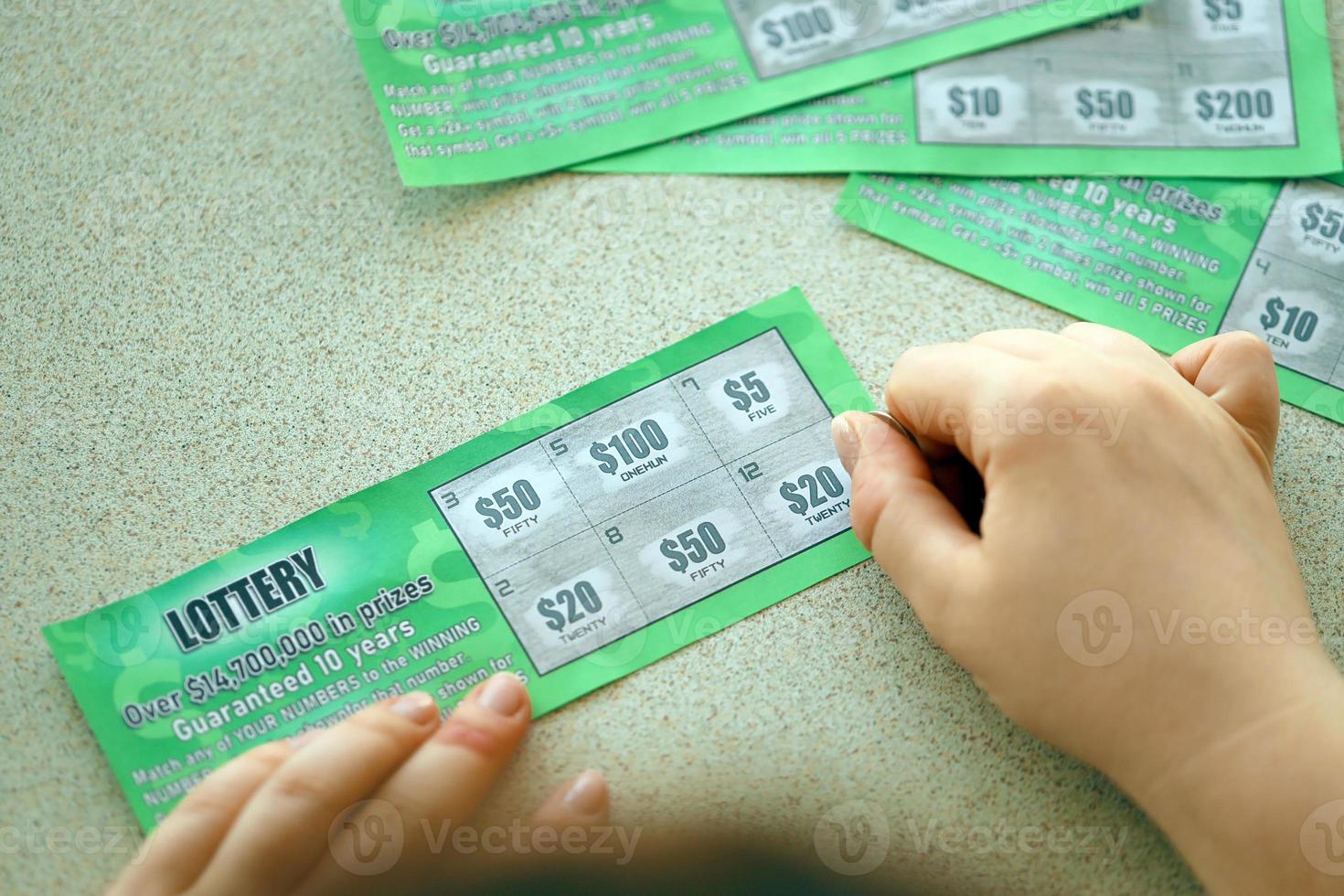 Close up view of silver coin in hand of gambler scratching fake lottery card. Lottery gambling concept, scratching cards lottery photo