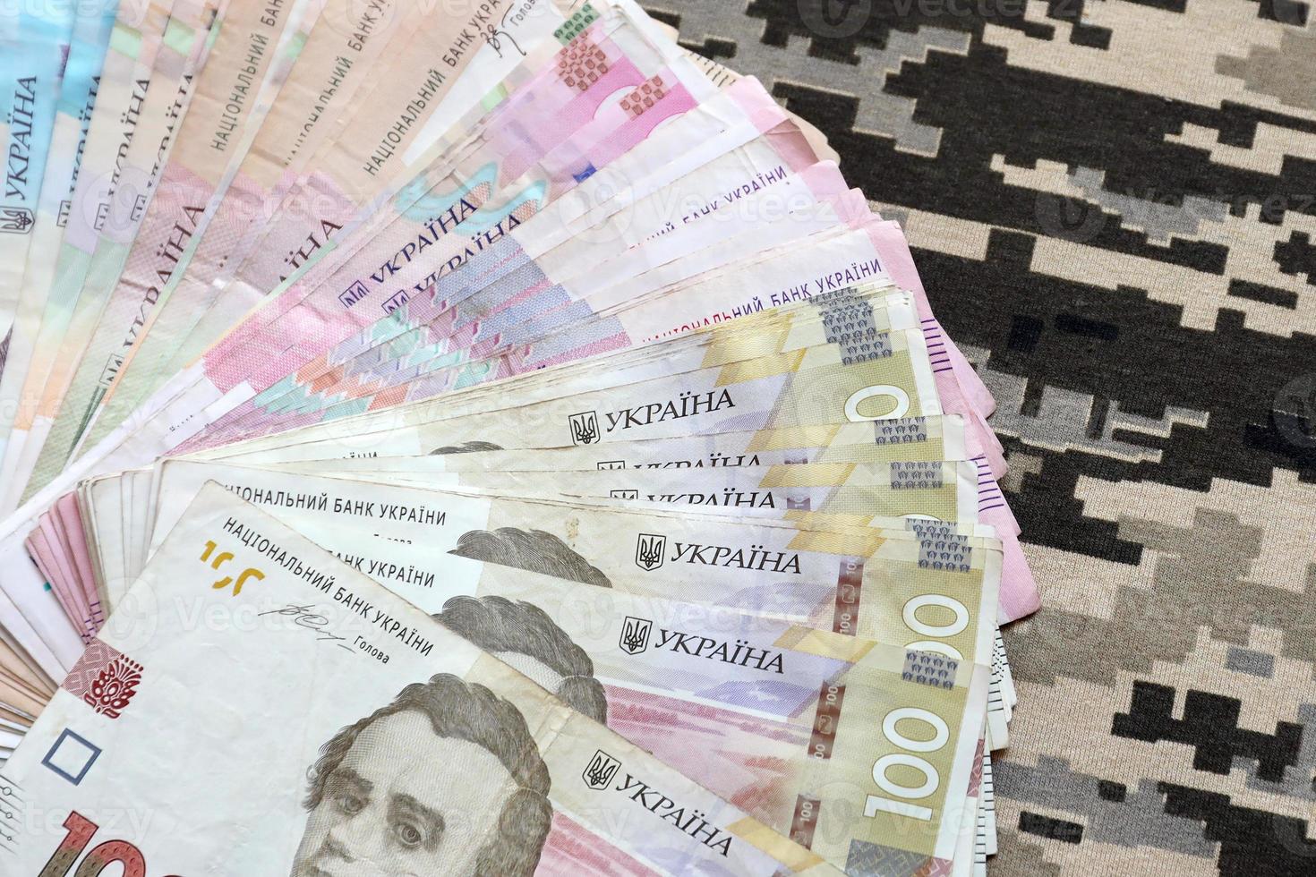 Ukrainian hryvnya bills on fabric with texture of Ukrainian military pixeled camouflage. Cloth with camo pattern in grey, brown and green pixel shapes photo