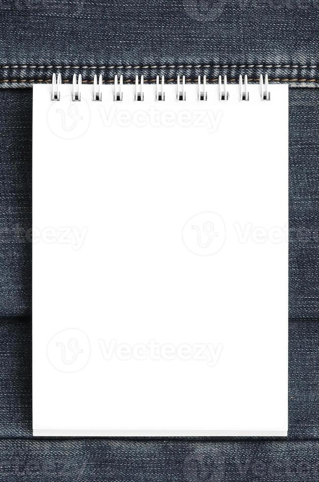 White notebook with clean pages lying on dark blue jeans background. Image with copy space photo