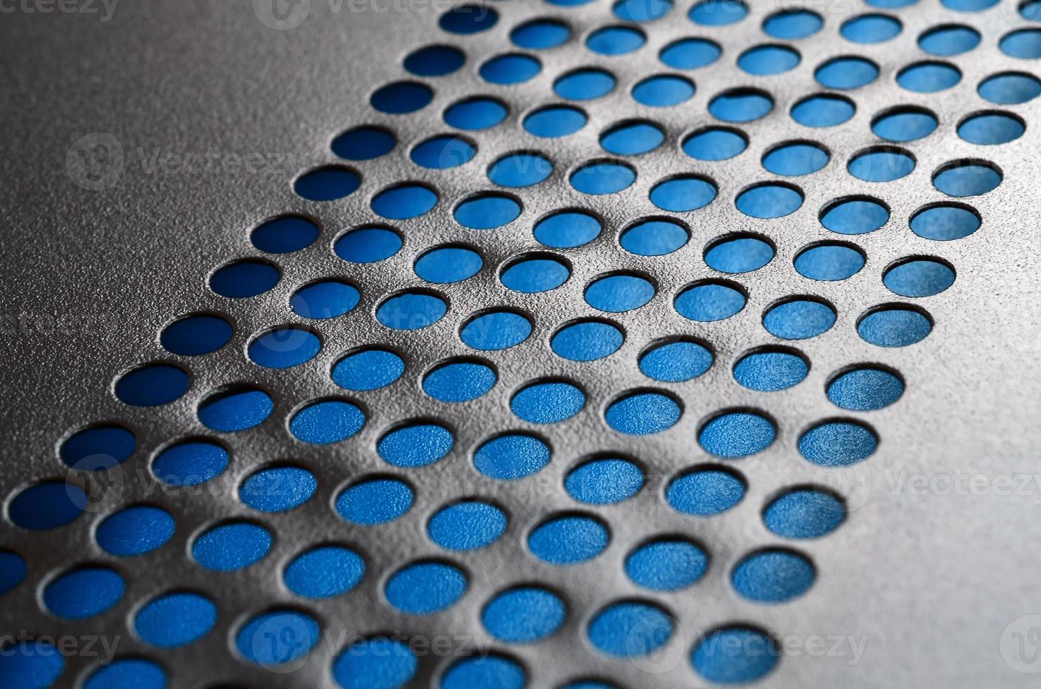 Black metal computer case panel mesh with holes on blue background. Abstract close up image photo