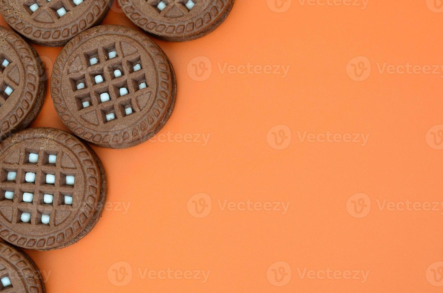 Detailed picture of dark brown round sandwich cookies with coconut filling on an orange surface. Background image of a close-up of several treats for tea photo