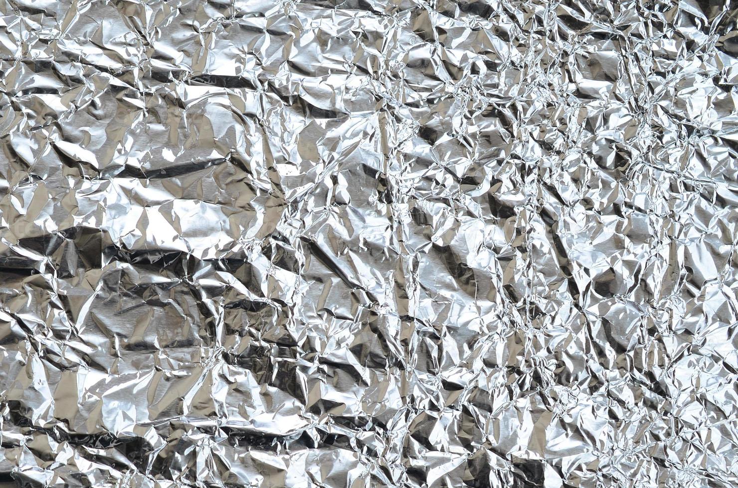 Thin wrinkled sheet of crushed tin aluminum silver foil background with shiny crumpled surface for texture photo