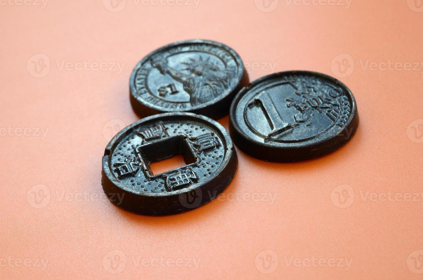 Three chocolate products in the form of Euro, USA and Japan coins lie on an orange plastic background. A model of cash coins in an edible form photo
