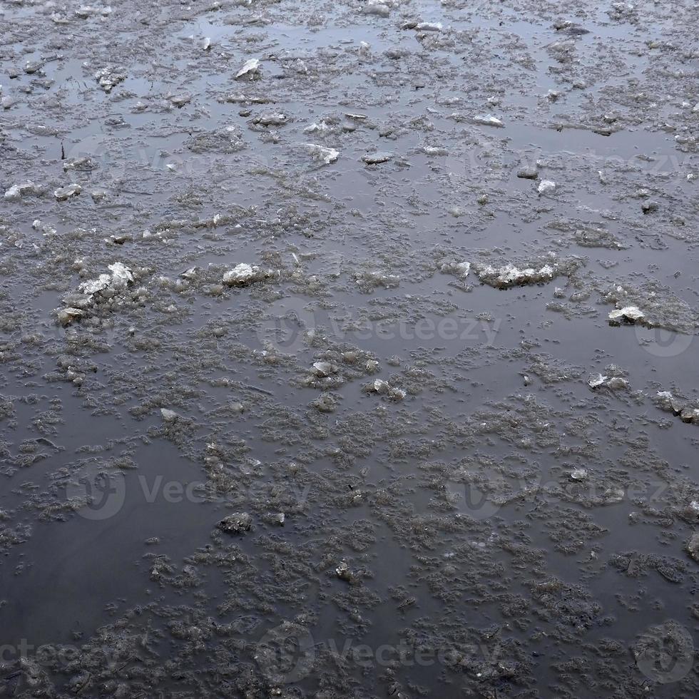 Damaged asphalt road with potholes, filled with water with ice, caused by freezing and thawing in winter. Bad road photo