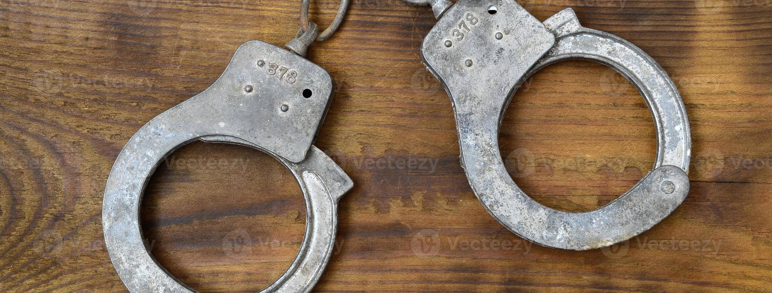 Old and rusty police handcuffs lie on a scratched wooden surface. The concept of an old crime photo