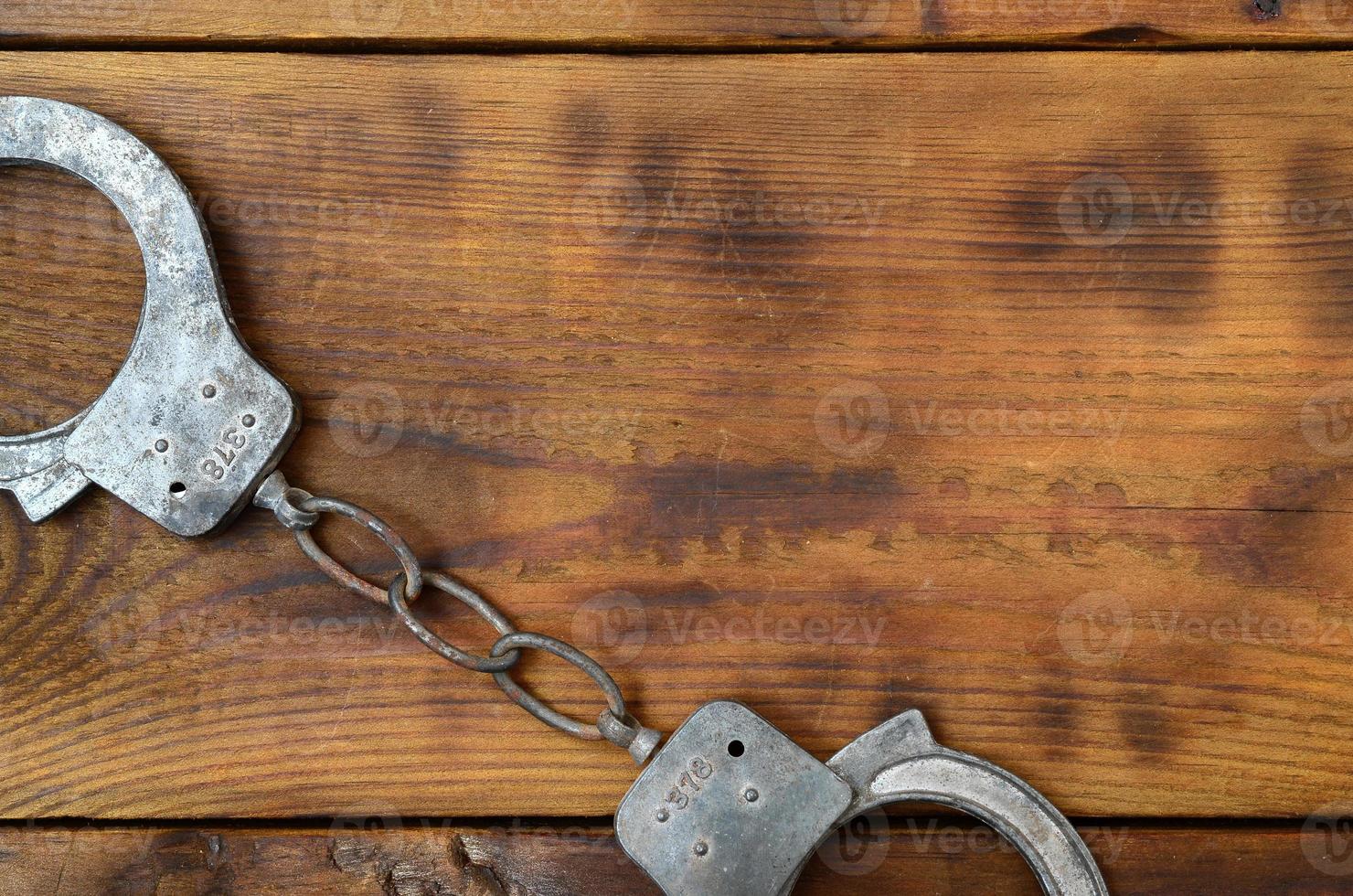 Old and rusty police handcuffs lie on a scratched wooden surface. The concept of an old crime photo